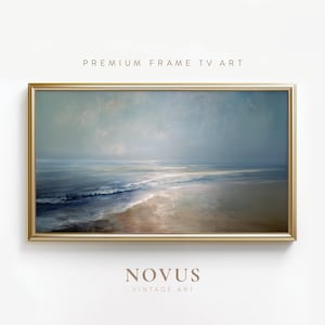 May include: A framed landscape painting of a beach scene with a gold frame. The artwork features a muted color palette of blues, browns, and whites, with the text "PREMIUM FRAME TV ART" and "NOVUS VINTAGE ART".