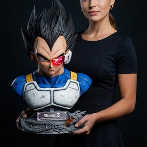 May include: A detailed bust of the Dragon Ball Z character Vegeta, featuring spiky black hair and a stern expression. The bust is blue, white, and gray, with a red visor. The base has the Dragon Ball Z logo.