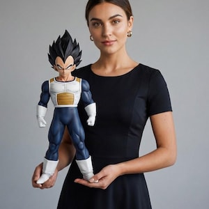 May include: A detailed figurine of the character Vegeta from the Dragon Ball Z anime series. The figure is in a dynamic pose, with a blue and white outfit, spiky black hair, and a determined expression. The figure is held by a person wearing a black dress.