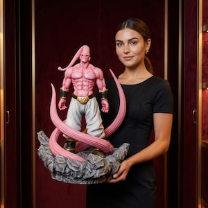 May include: A pink and white Majin Buu statue from the Dragon Ball Z anime series. The figure is muscular, with a pink body, white pants, and a gold belt. It stands on a gray rocky base.