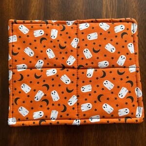 Könnte beinhalten: Ein rechteckiger, orangefarbener Stoffartikel zum Thema Halloween mit einem sich wiederholenden Muster aus weißen Geistern, schwarzen Monden und Sternen. Der Artikel ist in vier Abschnitte mit einem weißen Rand unterteilt.