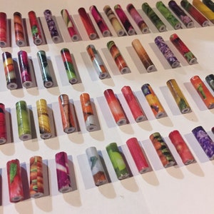 May include: A collection of colorful, patterned, cylindrical beads. The beads are made of paper and feature various designs, including fruits, vegetables, and flowers.