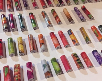 May include: A collection of colorful, patterned, cylindrical beads. The beads are made of paper and feature various designs, including fruits, vegetables, and flowers.