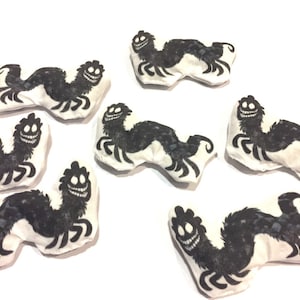 May include: Seven black and white plush toys shaped like a creature with a long body, four legs, and a large, toothy grin. The toys are on a white background.