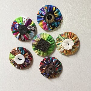 May include: Six colorful fabric circles with different buttons in the center. The circles are made of various fabrics with different patterns and colors. The buttons are all different shapes and sizes.
