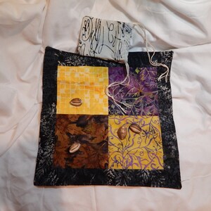 May include: A black and white fabric pouch with a patchwork design of yellow, purple, and brown squares. The pouch is filled with four small brown seashells.