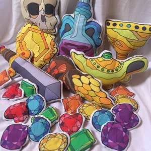 May include: A collection of colorful plush toys, including a skull, a genie lamp, a sword, and a variety of gems. The toys are arranged on a white surface.