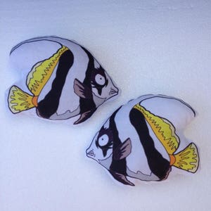 May include: Two black, white, and yellow fish-shaped pillows. The pillows are made of fabric and have a cartoon-like design.