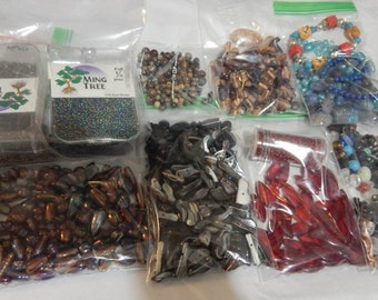May include: Assortment of beads in various colors and shapes, including clear, brown, red, blue, and black. The beads are packaged in clear plastic bags. Some bags have labels with the text "Ming Tree" and "Full 1/2 pound".
