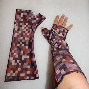 May include: A pair of brown and purple patterned arm warmers with a pixelated design. The arm warmers are made of a stretchy fabric and have a fitted design.