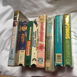 May include: A stack of six VHS tapes, including "Real Genius", "Samson", "Angermouse", "Blackstar", "Young Sherlock Holmes", and "The Complete Works of Bill Plympton:  Hamptoon's".