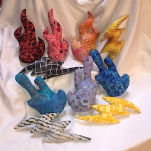 May include: A collection of ten handmade fabric flame and lightning bolt shapes. The shapes are made from different patterned fabrics in various colors, including red, orange, yellow, blue, and purple.