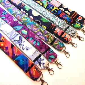 May include: A collection of colorful fabric lanyards with different patterns, each featuring a black trim and a gold metal swivel clasp.
