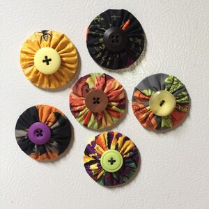 May include: Six fabric covered buttons with different patterns and colors. The buttons are round and have a flat back. The buttons are arranged in a circle on a white surface.