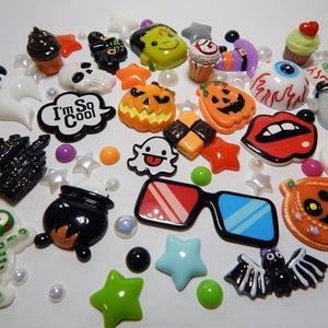 May include: A collection of Halloween themed resin cabochons, including pumpkins, ghosts, bats, a cauldron, a skeleton, a castle, a cupcake, a skull, a monster, a pair of 3D glasses, and a speech bubble that says "I'm So Cool".