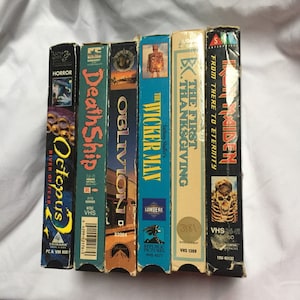 May include: A row of six VHS tapes, including "Octopus 2", "Death Ship", "Oblivion", "The Wicker Man", "The First Thanksgiving", and "Iron Maiden: From There to Eternity".