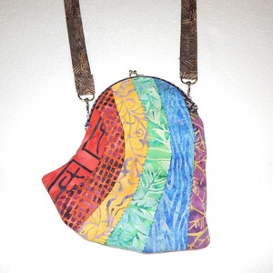 May include: A rainbow-colored fabric purse with a brown strap. The purse is made of patchwork fabric with different patterns and colors.