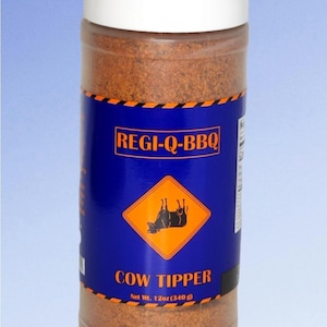 May include: A clear plastic container with a white lid filled with brown seasoning. The label is blue with the text "REGI-Q-BBQ" and "COW TIPPER". A yellow diamond graphic shows a silhouette of a cow. Net Wt. 12oz (340 g).