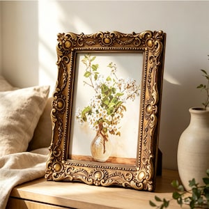 May include: A rectangular picture frame with an ornate, antique gold finish featuring intricate scrollwork and relief detailing. The frame holds a print of a clear glass vase filled with white flowers and green leaves on a table.
