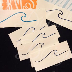 May include: Several white rectangular stickers with a blue wave design. The stickers are arranged on a black surface, with a few other stickers visible in the background. The wave design is a simple, stylized illustration.