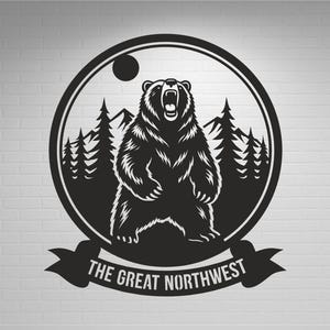 Può includere: Illustrazione in bianco e nero di un orso che ruggisce, circondato da una cornice circolare con pini, montagne e un sole. Il testo "THE GREAT NORTHWEST" è visualizzato su uno striscione sottostante. Il design è su un muro di mattoni bianchi.