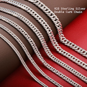 May include: Close-up of several sterling silver double curb chains of varying widths. The chains are displayed on a red and brown surface. The text "925 Sterling Silver Double Curb Chain" is visible in the upper right corner.