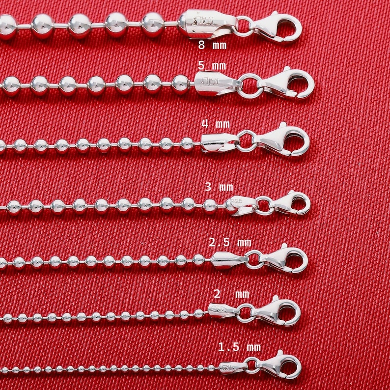 May include: Seven silver ball chains of varying thicknesses, ranging from 1.5 mm to 8 mm, each featuring a lobster claw clasp. The chains are arranged horizontally, with labels indicating their specific diameters in millimeters.