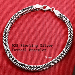 May include: A 925 sterling silver foxtail bracelet with a lobster claw clasp. The metal chain features a woven, braided link design with a polished finish. The bracelet is marked with 925 and measures 5 mm in width as indicated by the text.