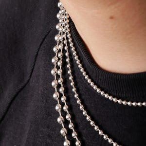 May include: A layered necklace set consisting of four distinct silver-toned ball chains. The chains feature varying bead sizes, ranging from small, uniform spheres to larger, graduated metallic balls, all resting against a black fabric background.