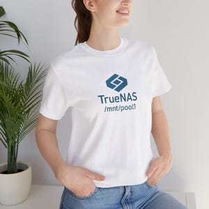 May include: White t-shirt with a blue logo and text that reads "TrueNAS /mnt/pool1". The shirt has short sleeves and a crew neck. The design is centered on the chest.