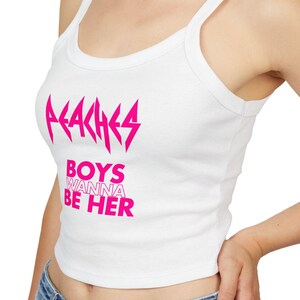 Puede incluir: Camiseta sin mangas blanca con el texto "PEACHES" encima de "BOYS WANNA BE HER" en rosa brillante. La camiseta tiene cuello redondo y tirantes finos.