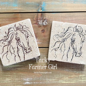 May include: Two beige stone coasters with black line drawings of a horse's head. The coasters are square and have a rough texture. The text "Tacky Farmer Girl" is printed below the coasters.