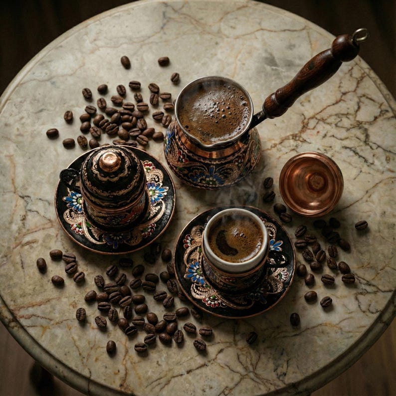 以下が含まれることがあります： 大理石のテーブルに置かれたトルココーヒーのセットの静物画。銅製のコーヒーポット、ソーサー付きの小さなカップ2つ、蓋付きのカップがあり、すべて複雑なデザインで飾られています。コーヒー豆がカップの周りに散らばっています。