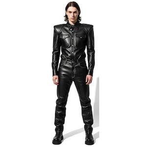May include: A black leather shirt with shoulder pads and two chest pockets, paired with matching black leather pants. The outfit features white stitching and is worn with black boots. The model is standing against a white background.