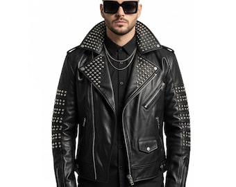 Può includere: Giacca in pelle nera con borchie argentate su colletto, spalle e maniche. La giacca presenta un classico stile biker con revers a lancia, chiusura asimmetrica con zip e più tasche. È visibile una collana a catena argentata.