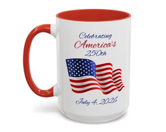 Könnte beinhalten: Weißer Keramikbecher mit rotem Innenraum und Henkel. Der Becher zeigt den Text "Celebrating America's 250th" und "July 4, 2026" zusammen mit einem Design der amerikanischen Flagge.