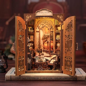 May include: A miniature wooden bookshelf diorama with openwork doors, featuring a detailed interior scene of a cozy reading nook. The diorama includes a table, chair, books, and a warm, inviting glow from the interior lighting. The sign on top reads "Bookshop Memories".
