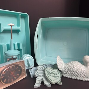 May include: A collection of vintage kitchen items in a light blue color, including a container, a hand-operated food chopper, a timer, a clock, cookie cutters, and a ceramic turkey figurine. The clock has a black face.