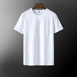 May include: A plain white crew neck t-shirt hanging on a wooden hanger. The short-sleeved shirt is made of a smooth, opaque fabric. The background is a gradient of gray and black.