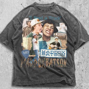 May include: Dark gray t-shirt featuring a collage of images with the text "I Need a Truck" and "Maddox Batson." The design includes photos of a person wearing a hat and playing a guitar. The shirt has a vintage, distressed look.