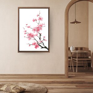 Puede incluir: Una impresión artística enmarcada que presenta una pintura a la acuarela de una rama de cerezo en flor con flores rosas y ramas oscuras sobre un fondo blanco. La obra de arte está en un marco de madera marrón.