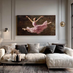 May include: A large rectangular canvas print depicts a ballerina in mid-air, wearing a flowing pink dress. The artwork is set against a dark brown, textured background. The print is displayed in a living room with a neutral color palette.