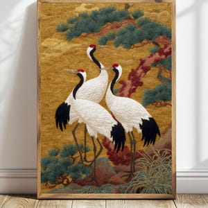 May include: A framed artwork featuring three white cranes with black wingtips and red head markings. The birds stand amidst a detailed landscape with a golden background, green foliage, and a reddish-brown tree trunk. The artwork is in a wooden frame.