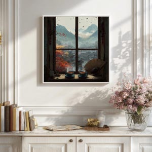 Puede incluir: Una impresión enmarcada que representa un paisaje sereno visto a través de una ventana. La obra de arte presenta una cordillera, un paisaje urbano y dos tazas de té turquesas. Un abanico decorativo descansa en el alféizar. La escena está enmarcada por un borde blanco.