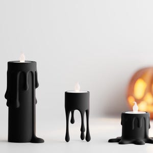 Puede incluir: Tres candelabros negros con diseño de cera goteando, cada uno con una luz LED parpadeante. Una calabaza naranja tallada está en el fondo. Decoración de Halloween.