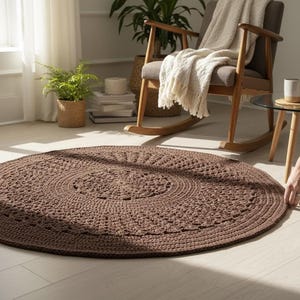 May include: A round, brown, crocheted rug with a detailed pattern. The rug is placed on a light-colored wooden floor. The rug's diameter is approximately 4 feet.