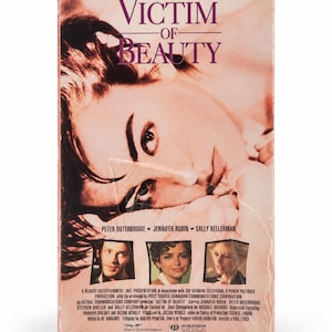 Op de afbeelding: Een VHS-cassette van de film Victim of Beauty. De hoes toont een close-up van een gezicht in sepia-tinten, de titel in paarse letters en de slogan: Some women you can't resist... some you can't survive. Inclusief foto's van de cast.