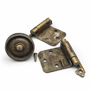 May include: An assortment of antique brass hardware components, including a round cabinet knob, two hinges, and two screws. The hardware has a weathered, aged appearance, suggesting vintage or reclaimed use. The items are arranged on a white background.