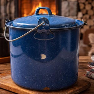 May include: A blue speckled enamelware pot with a lid and handle, sitting on a wooden cutting board. The pot has a metal handle and a matching lid. The background features a fireplace with a warm fire and a wooden surface.