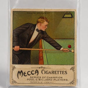 May include: Vintage Mecca Cigarettes trading card featuring Calvin Demarest playing billiards. The card shows a man in a suit aiming with a cue stick at a red and white billiard ball on a green table. The card is in a protective sleeve.